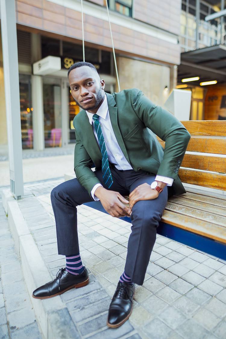 Man in green suit and striped socks sitting on bench outside