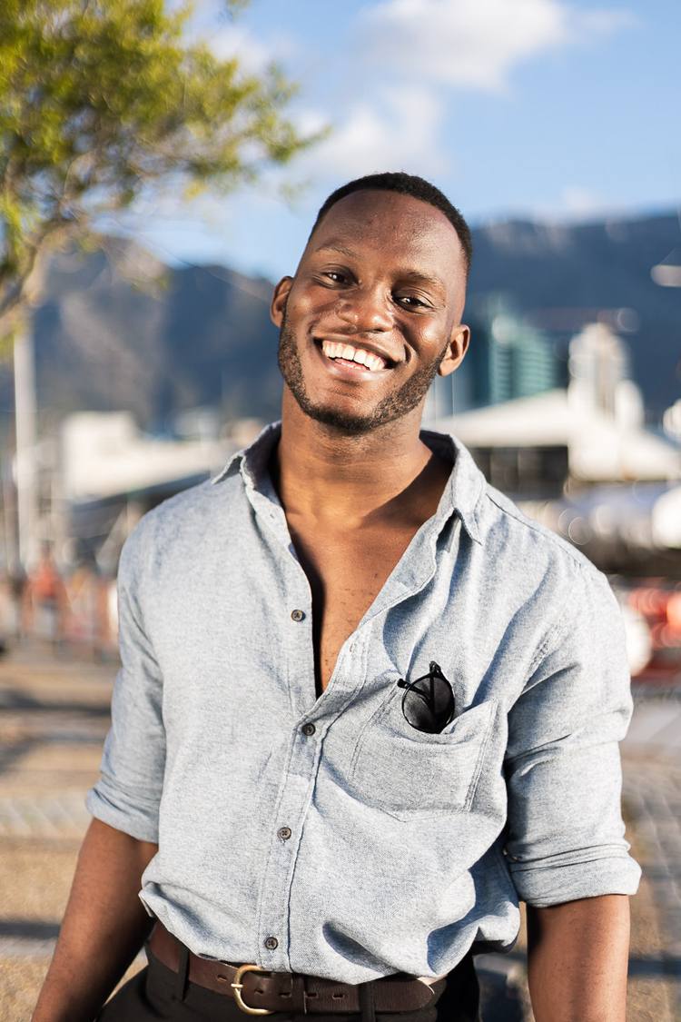 Man smiling with sunglasses in shirt pocket, mountains in background