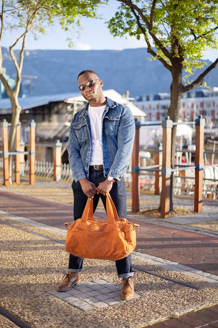 Man in denim jacket and sunglasses holding orange bag on a city street