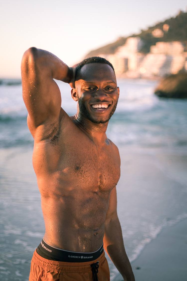Man smiling at camera with arm behind head on beach with ocean in background