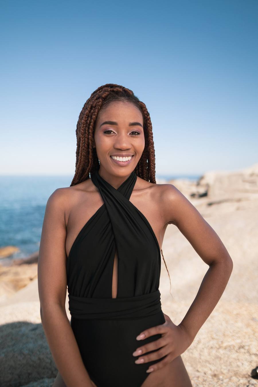 Woman in black swimsuit standing on beach with ocean in background