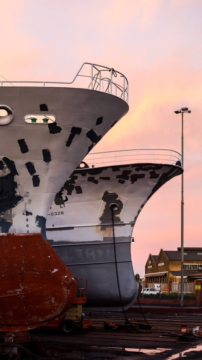Two large ships with faded paint and chains in a dockyard at dusk