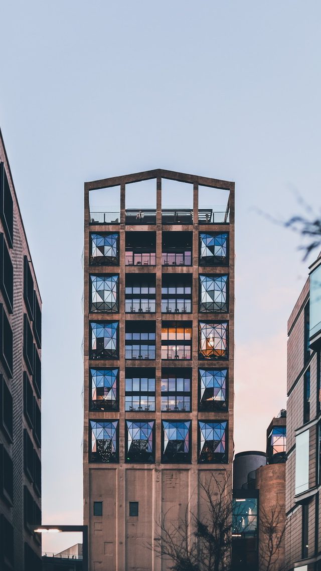 A tall building with many windows and balconies, surrounded by other buildings