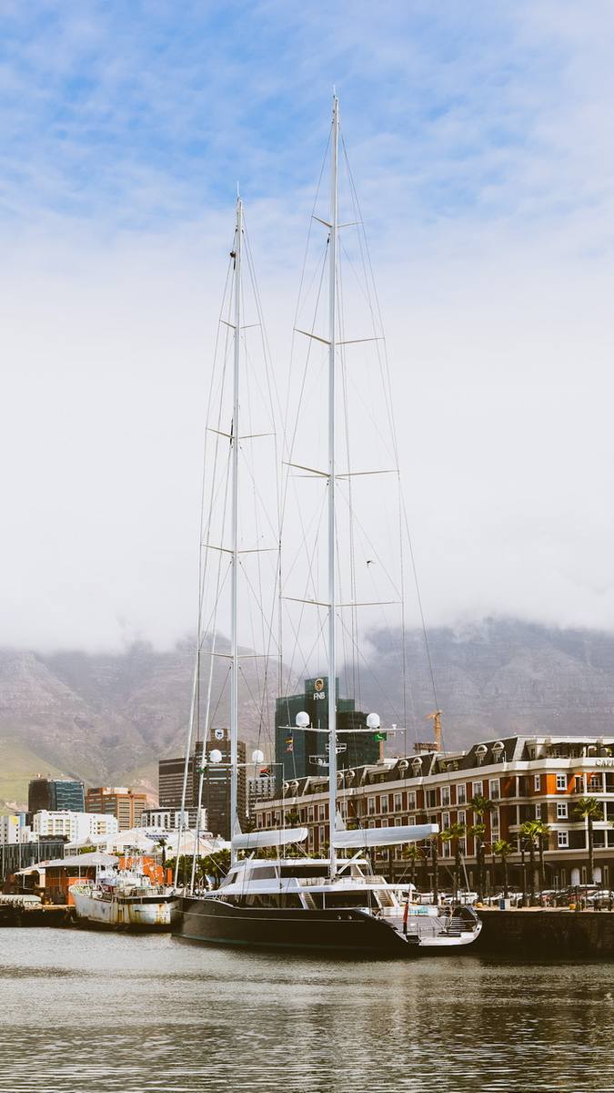 Two tall white masted boats in the water with buildings and mountains in the background