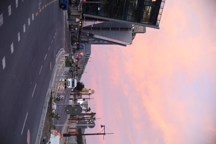 A city street with buildings and a pink sky at sunset