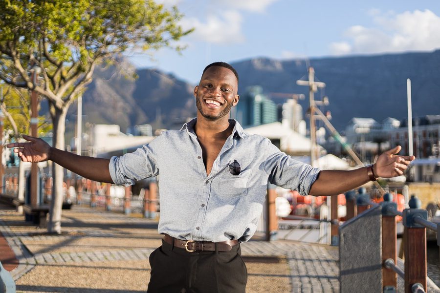 Man smiling with arms outstretched in front of a harbour