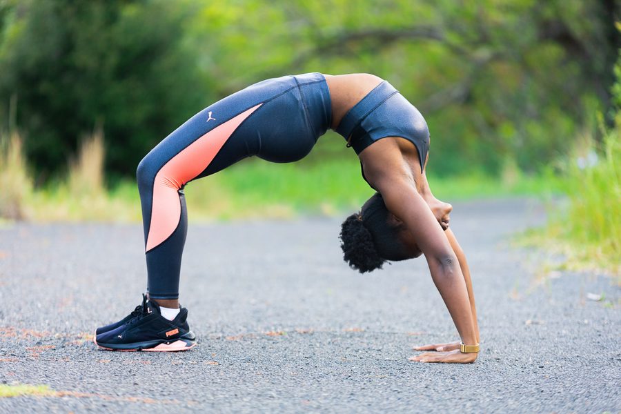 Woman in sports gear performing a back bend on a road with trees in the background