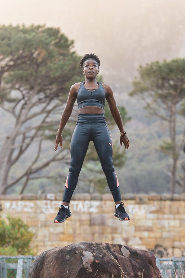 Woman in sports gear jumping over rock in outdoor setting