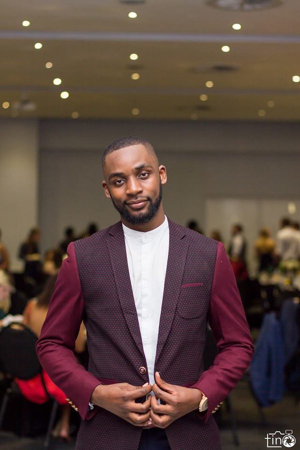 Man in maroon suit and white shirt standing in a room with other people
