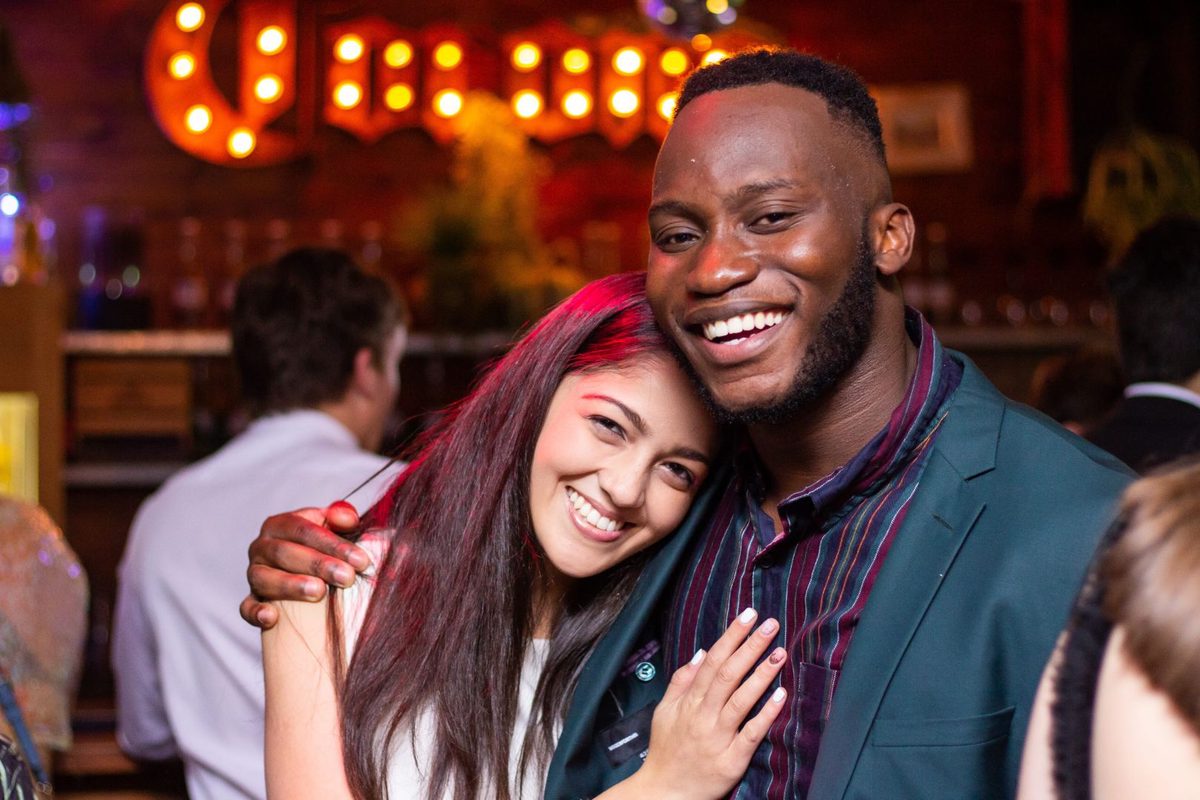 A smiling couple in a bar, the man's hand on the woman's waist.