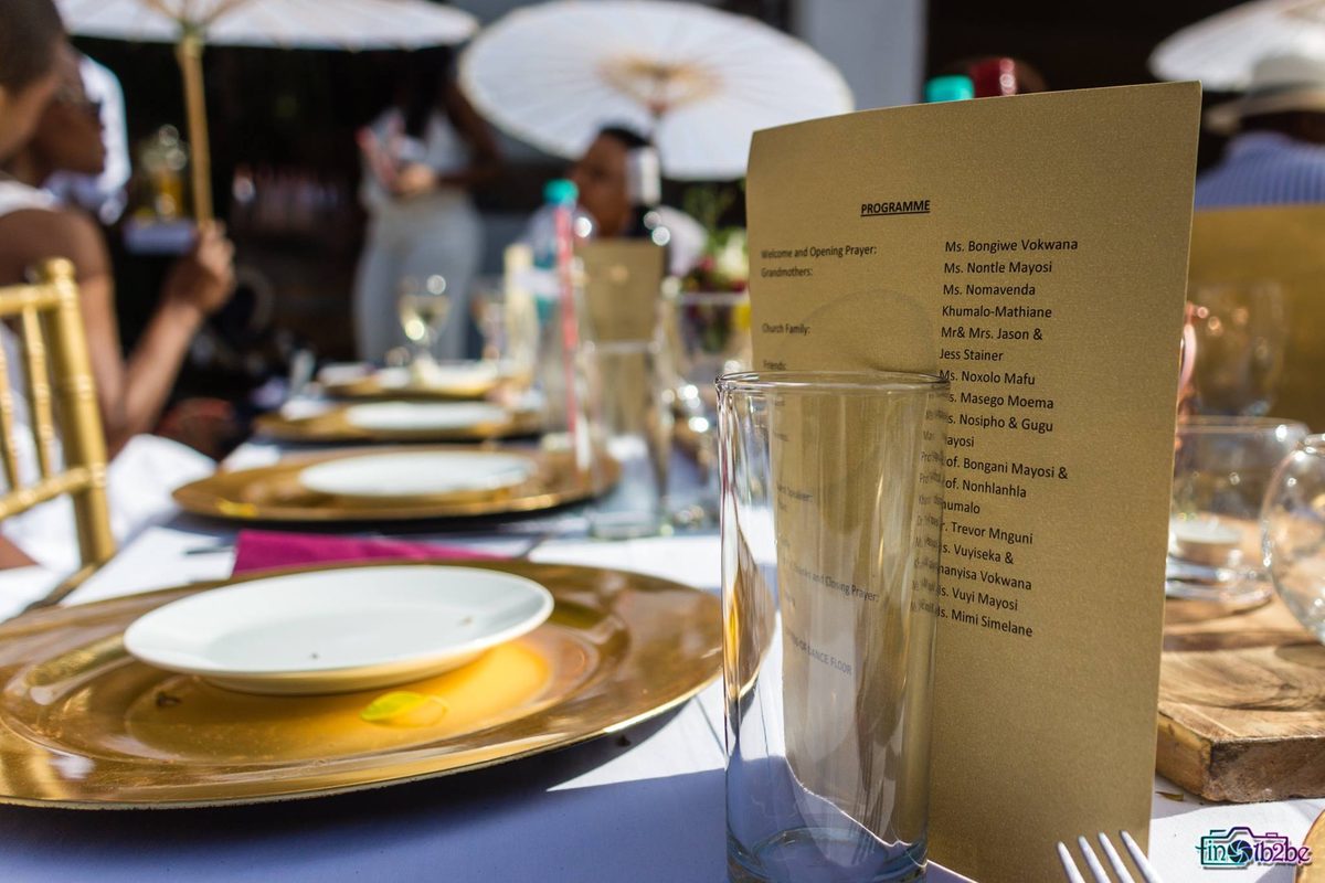 A table set for a wedding reception with a menu card and gold plates
