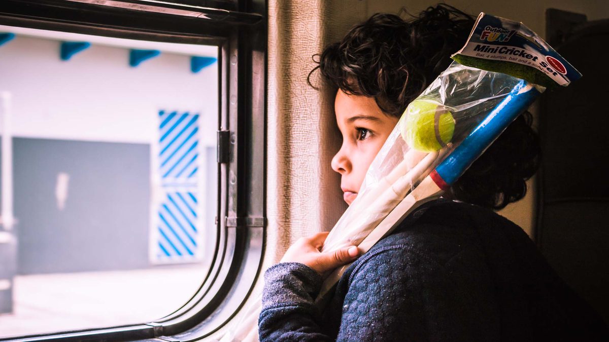 Child holding a mini cricket set, looking out of a window