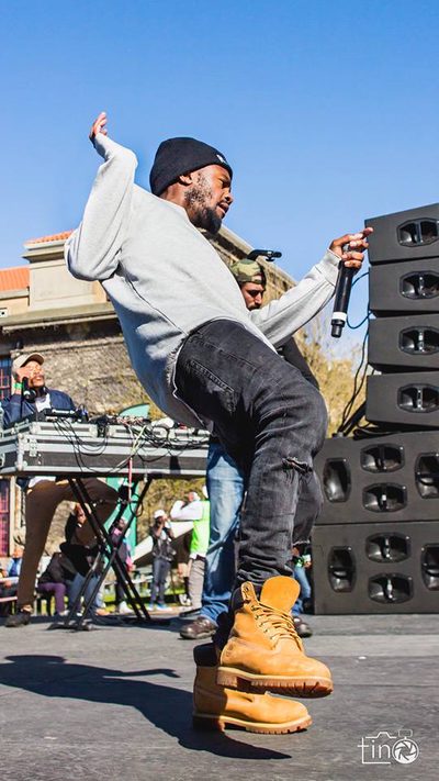 A man in a grey hoodie and jeans performs on stage with a microphone.